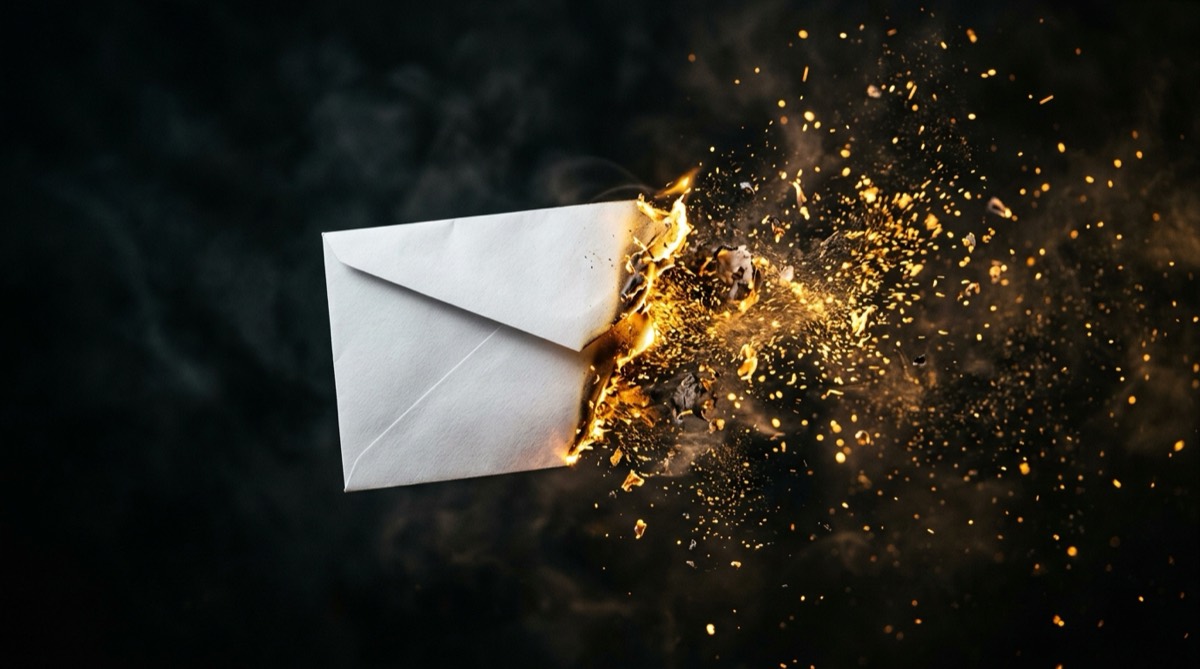 A white paper envelope dissolving into glowing embers and ash in mid-air.